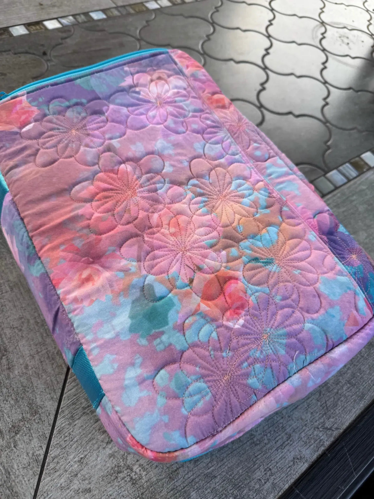 A quilted fabric bag with a purple, pink, and blue floral pattern.