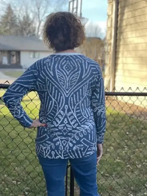 A person from behind wears a blue long-sleeved shirt with a white geometric pattern.