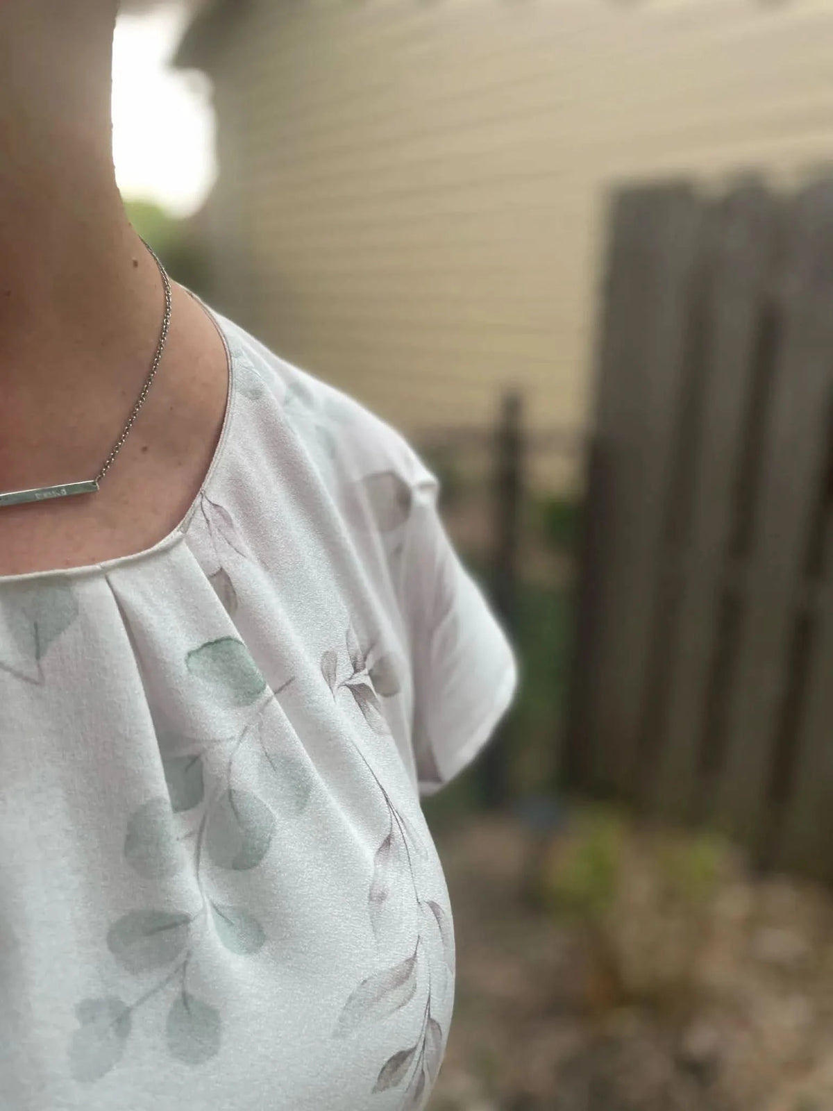 A person wears a light-colored top with a subtle eucalyptus leaf pattern.