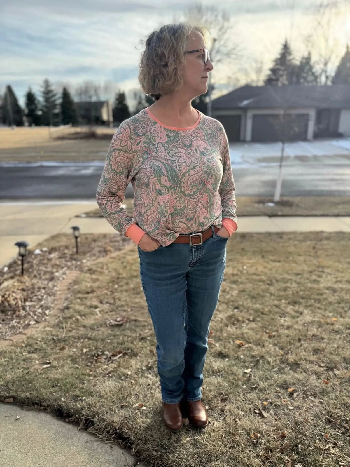 A woman wears a long-sleeved paisley shirt with jeans and brown boots.