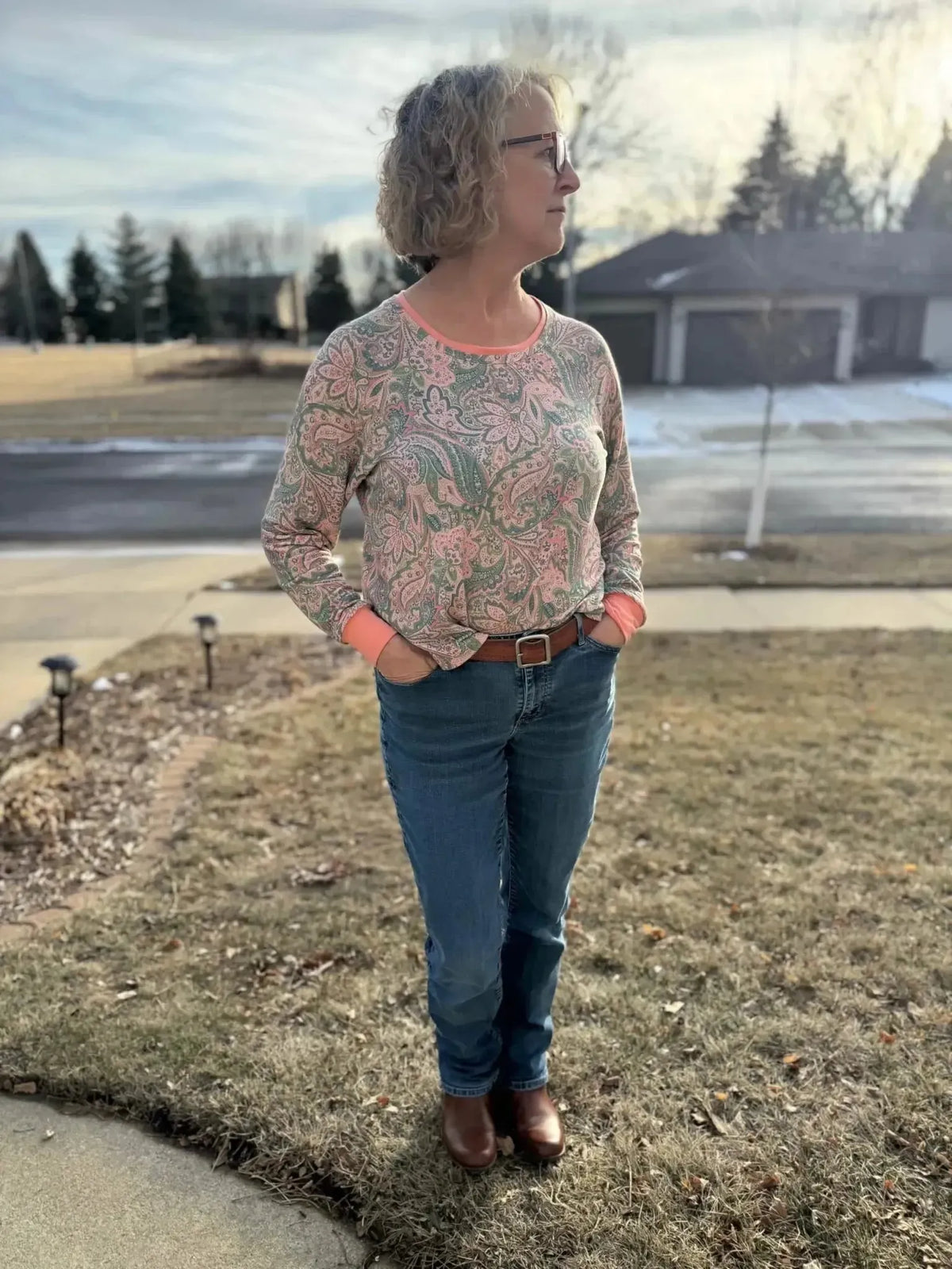 Woman wearing a pink and green paisley boho long-sleeve top with jeans outdoors.