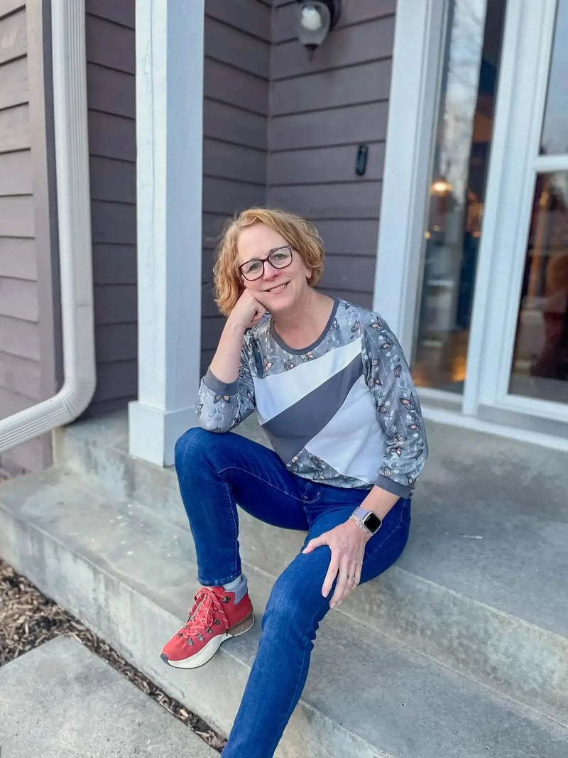 A woman in a butterfly-print shirt and jeans sits on concrete steps.