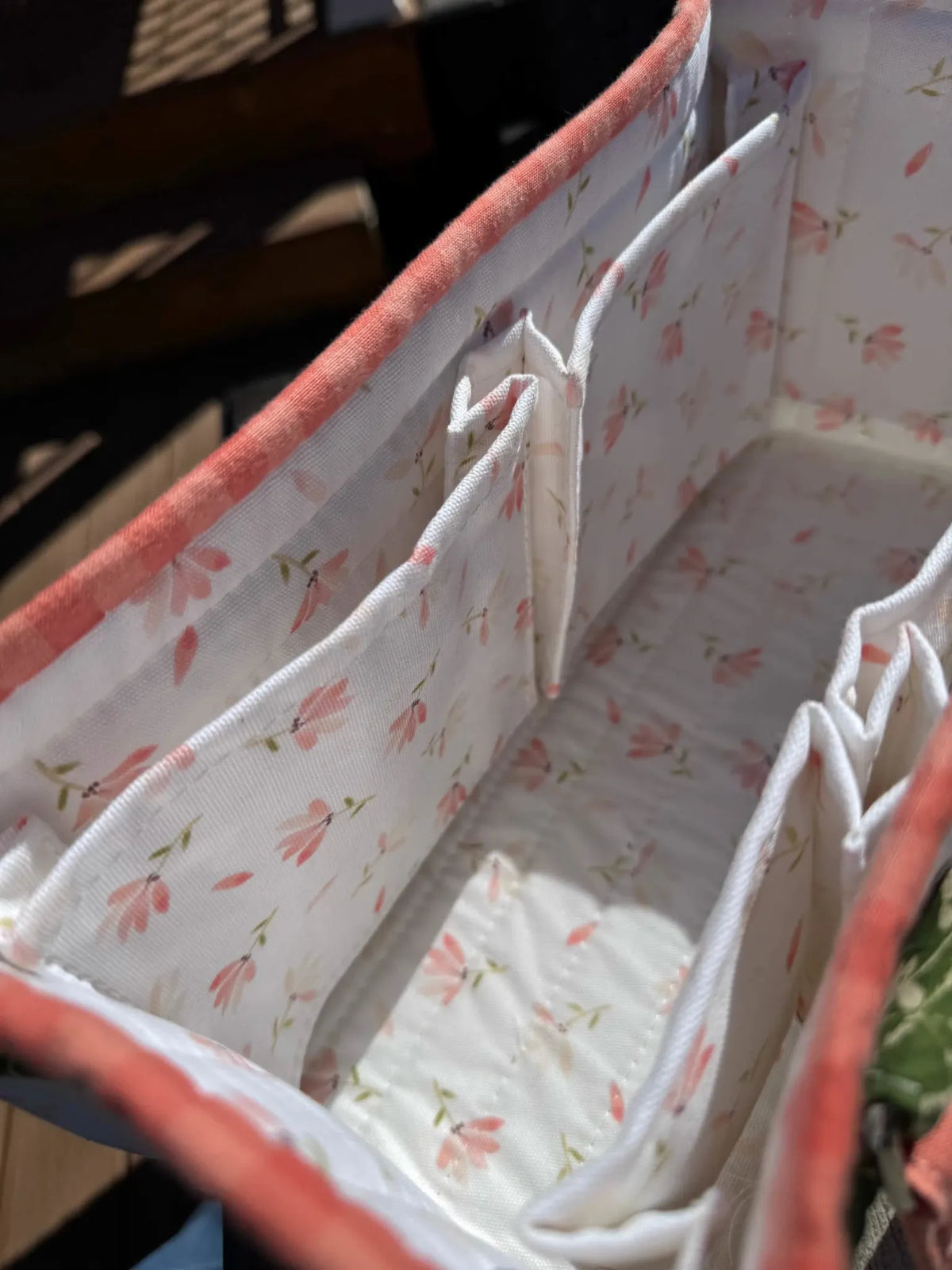 A fabric organizer with multiple compartments, featuring a white background with pink flowers.
