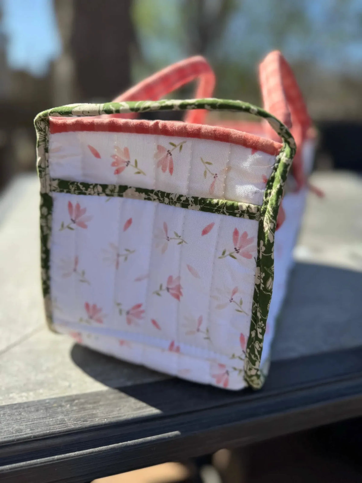 Quilted fabric basket with pink flowers and green trim.