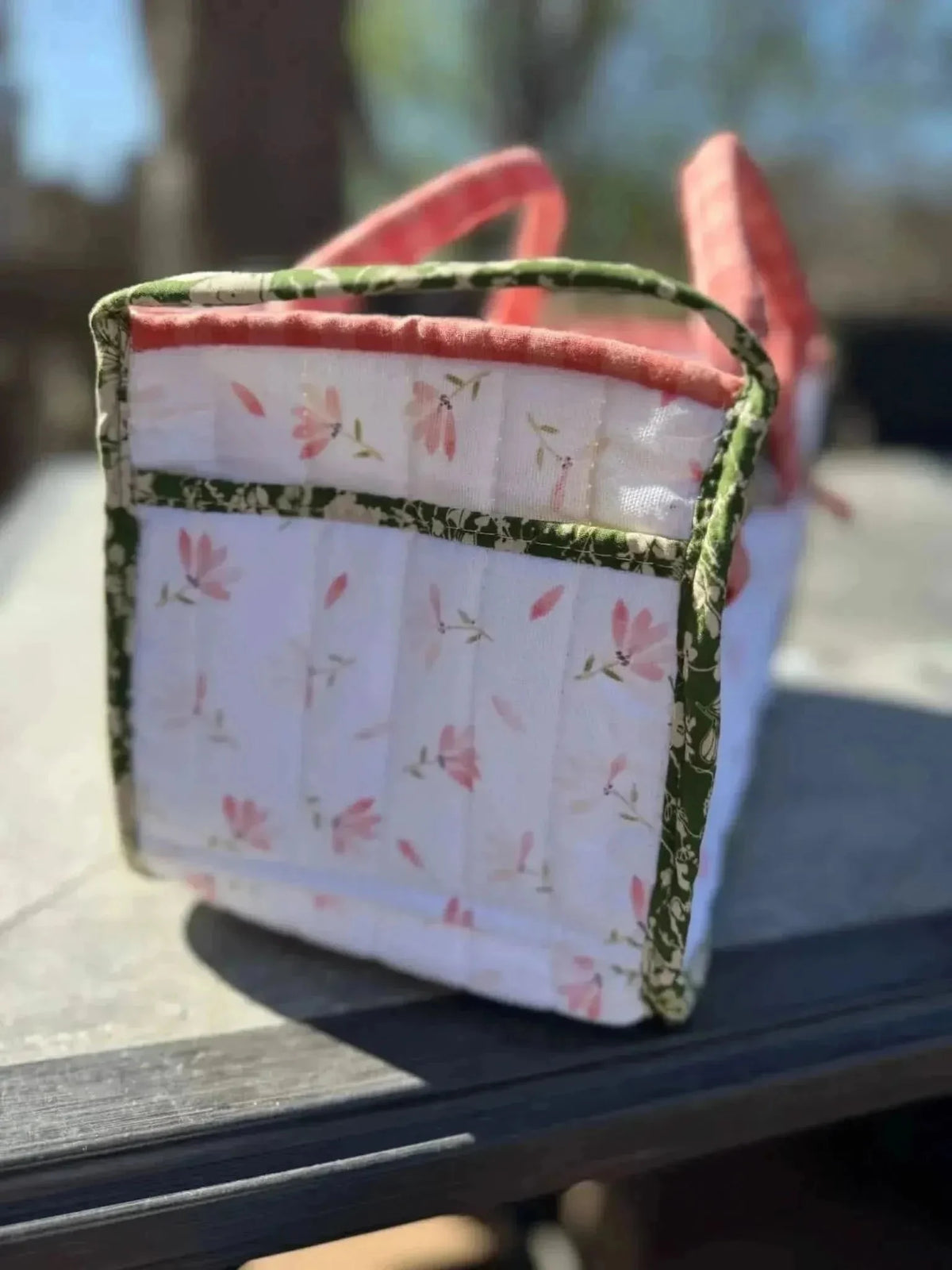 White tote bag with pink floral print and green trim on a wooden surface.