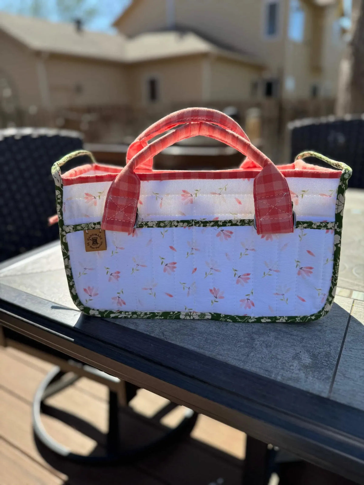 A handmade fabric tote bag with pink flowers, green trim, and red gingham handles.