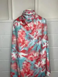 Fabric with a red, teal, and white tie-dye pattern is draped on a mannequin.
