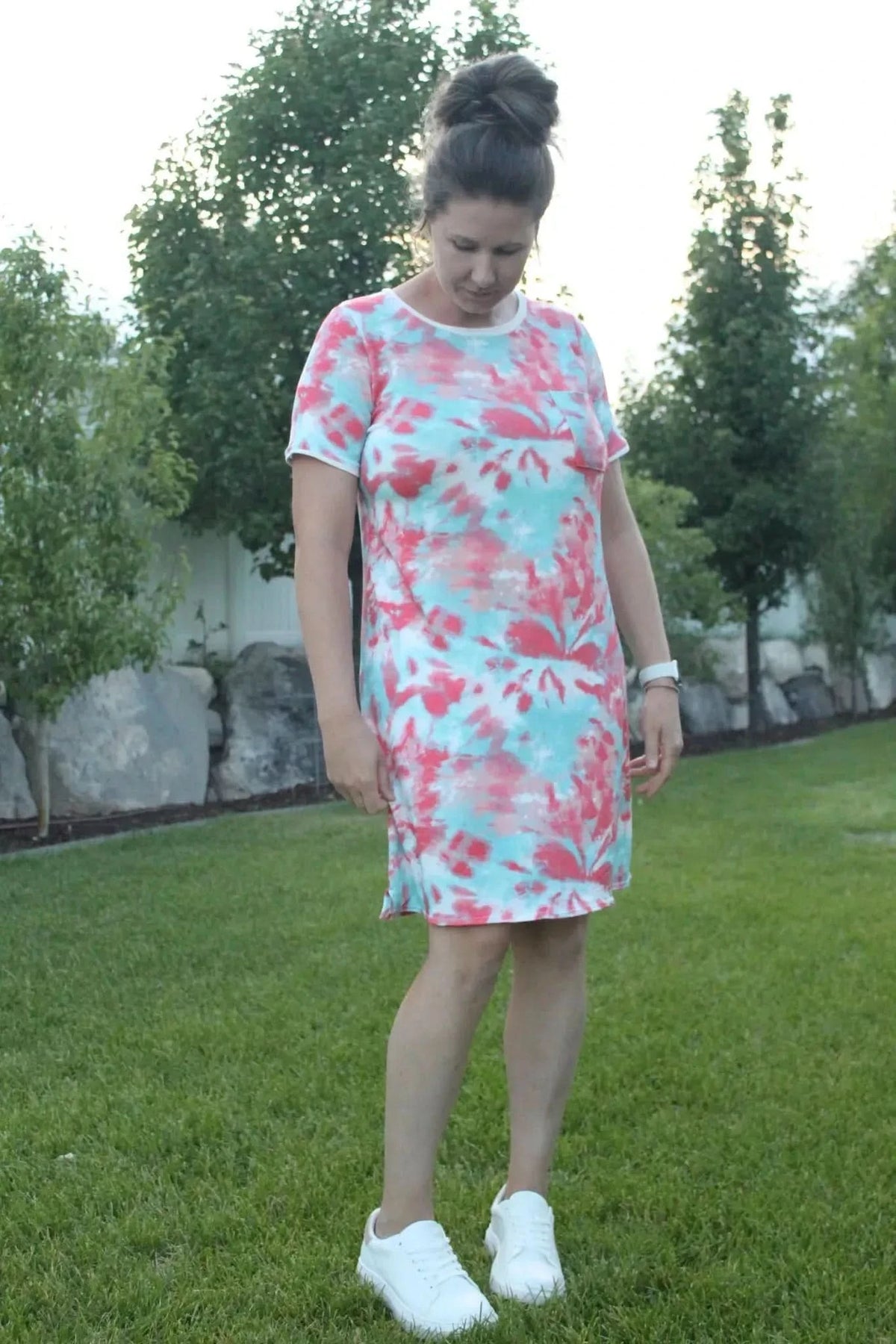A woman wears a tie-dye dress in shades of pink and blue with white sneakers.
