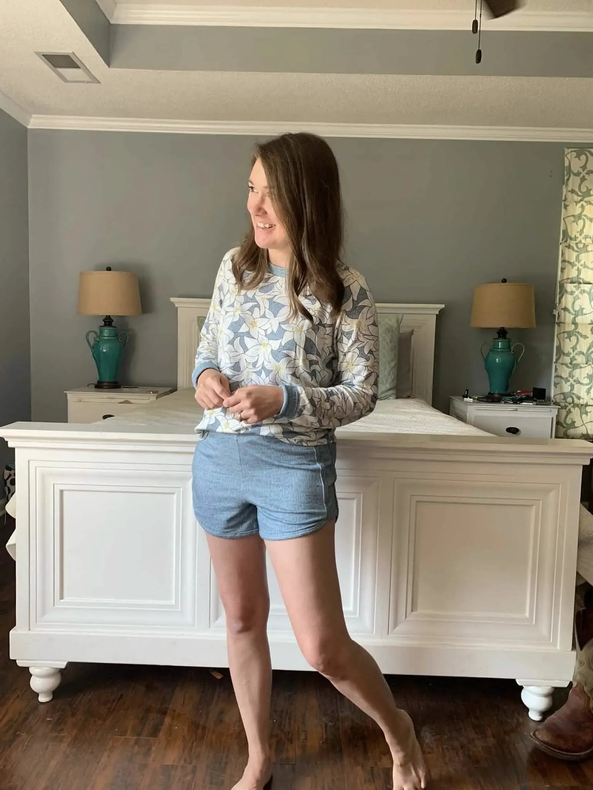 A woman wears a blue and white floral long-sleeve top and blue shorts.
