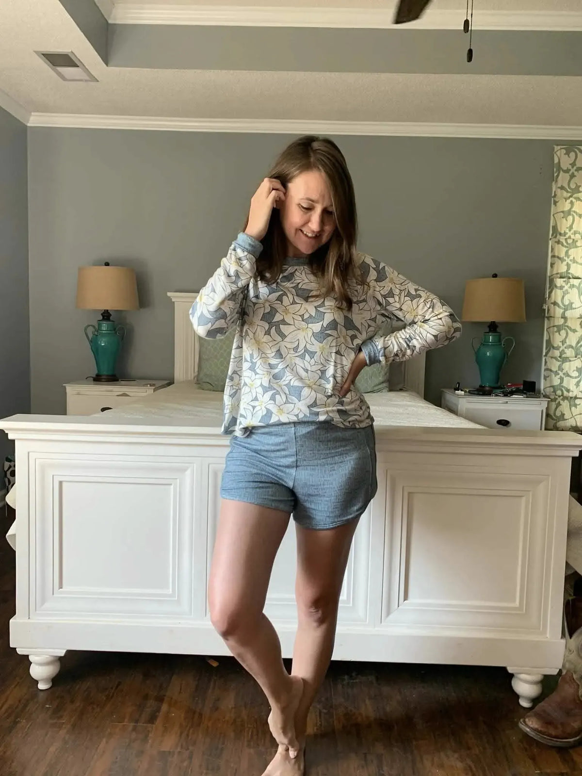 A woman wears a blue floral long-sleeve top and blue shorts.