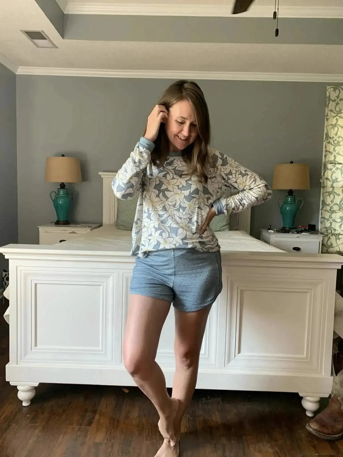 A woman wears a long-sleeved shirt with a blue and white floral print and blue shorts.