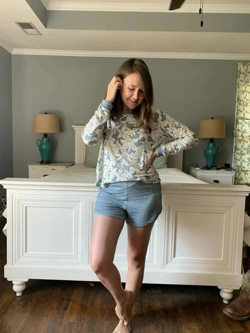 A woman wears a long-sleeved shirt with a blue and white floral print and blue shorts.