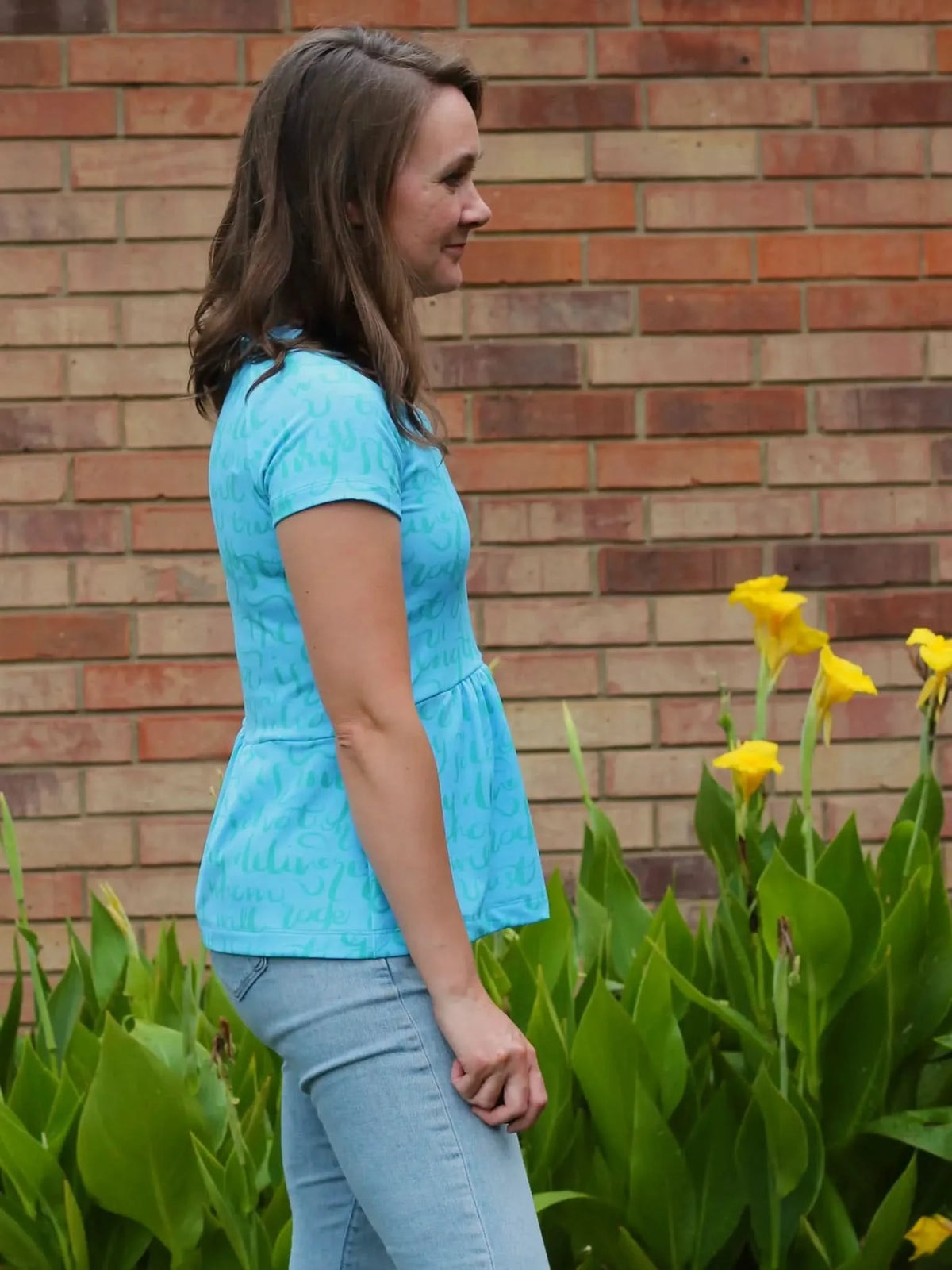 A woman in a light blue peplum top with subtle text stands in profile.