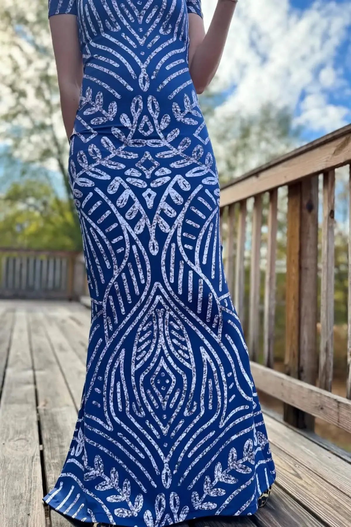 A person wearing a blue dress with a white and gray art deco pattern.