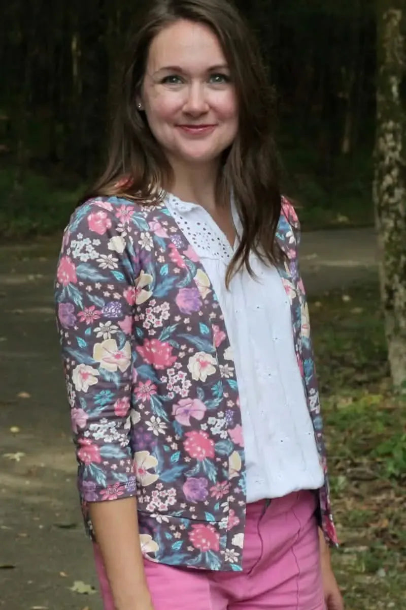A woman wears a maroon floral cardigan over a white top and pink pants.