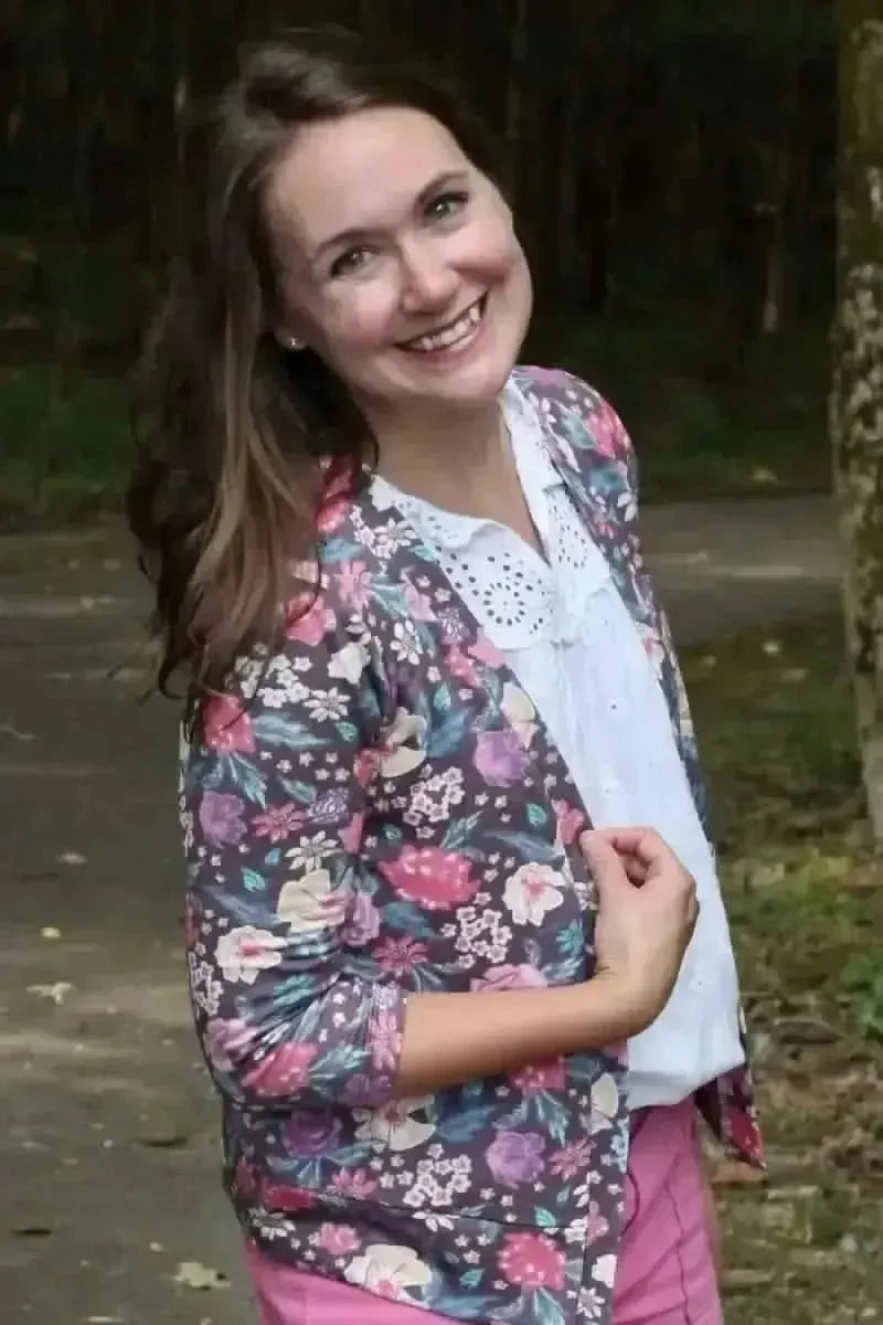 Woman modeling a maroon floral print blouse with botanical garden theme in a forest.