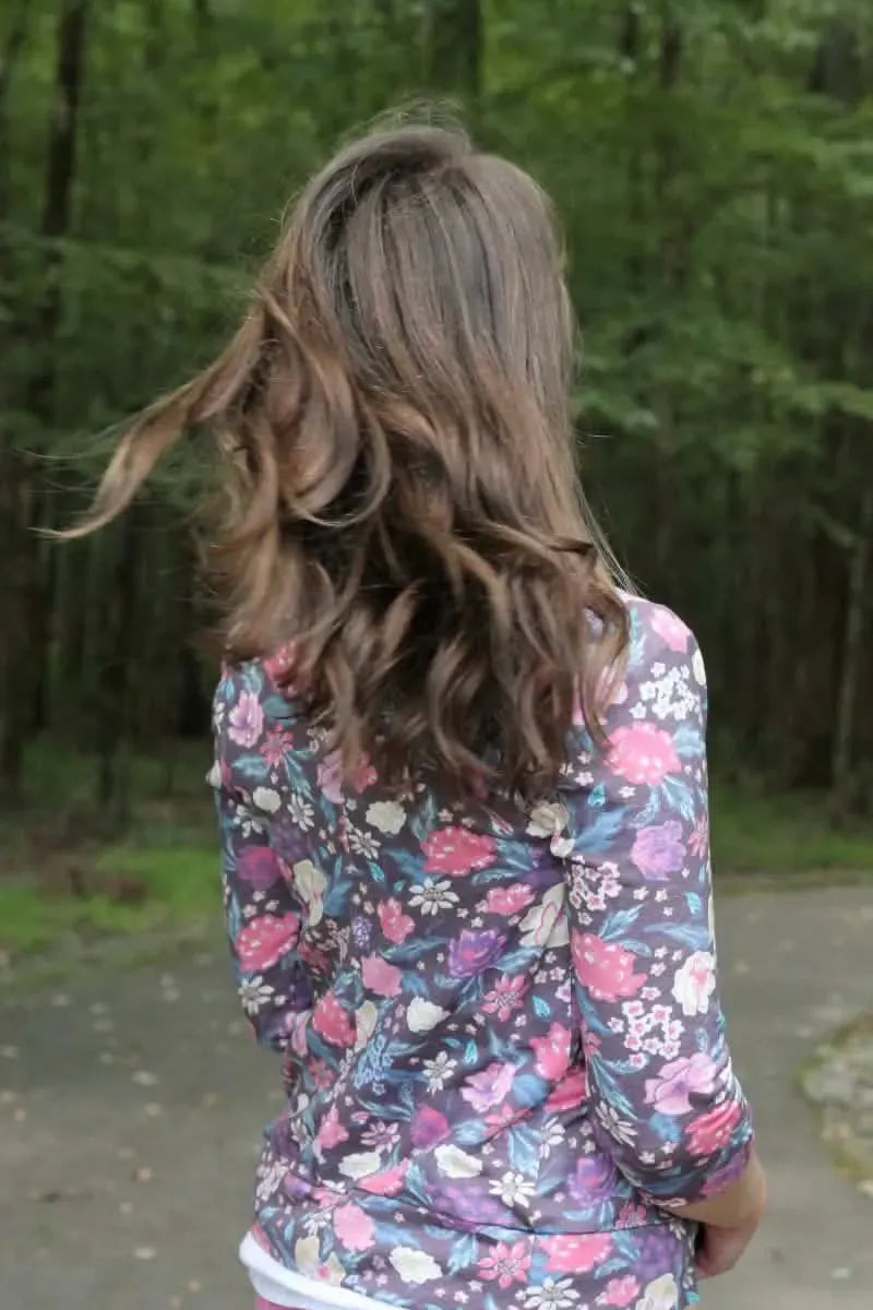 A person with long, wavy brown hair wears a maroon floral top.