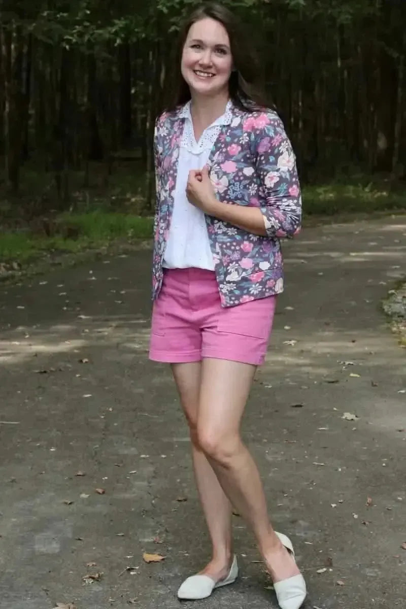 A woman wears a maroon floral print jacket, white top, and pink shorts.