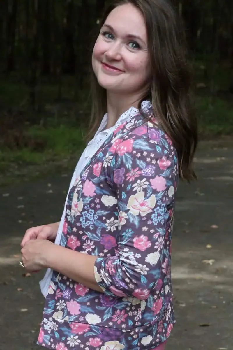 A woman wears a maroon floral print top with a white lace-trimmed shirt underneath.