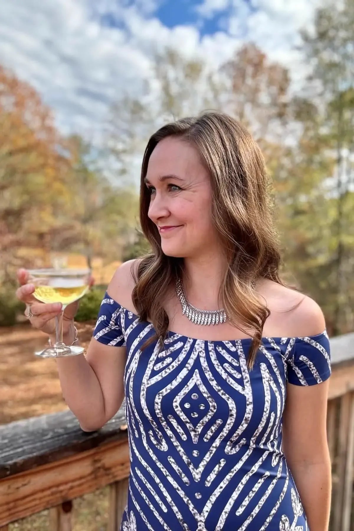 A woman in a blue and white patterned off-the-shoulder dress holds a glass of champagne.