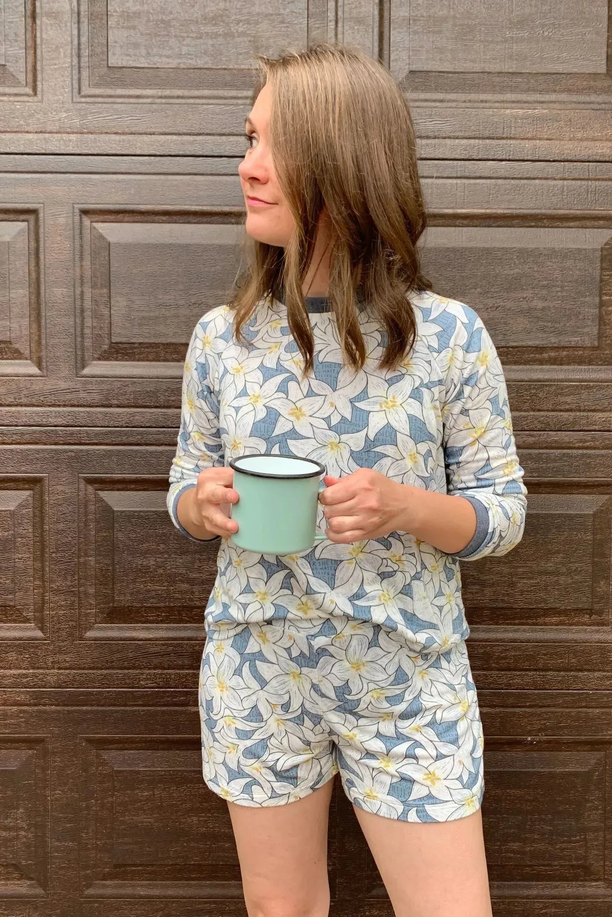 A woman wears a blue and white floral print top and shorts, holding a mint green mug.