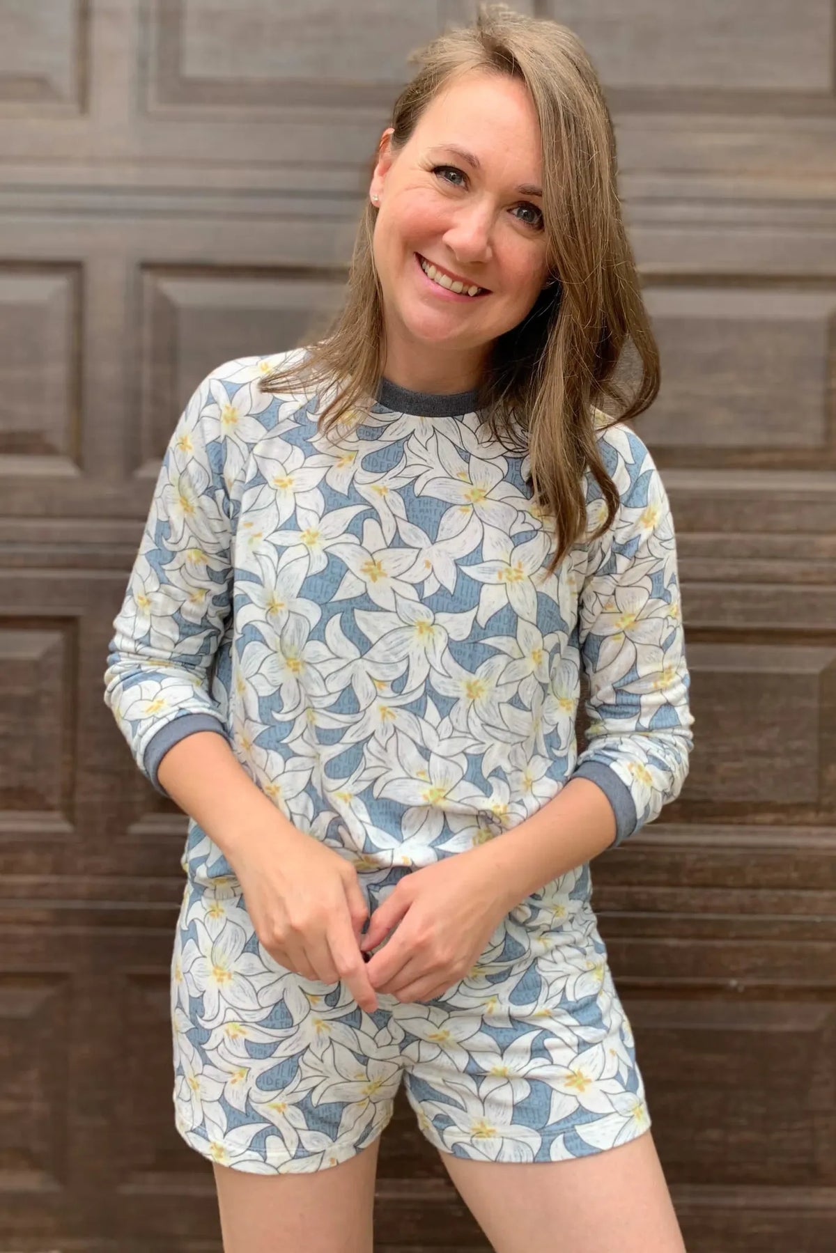 A woman smiles, wearing a blue and white floral print top and shorts.