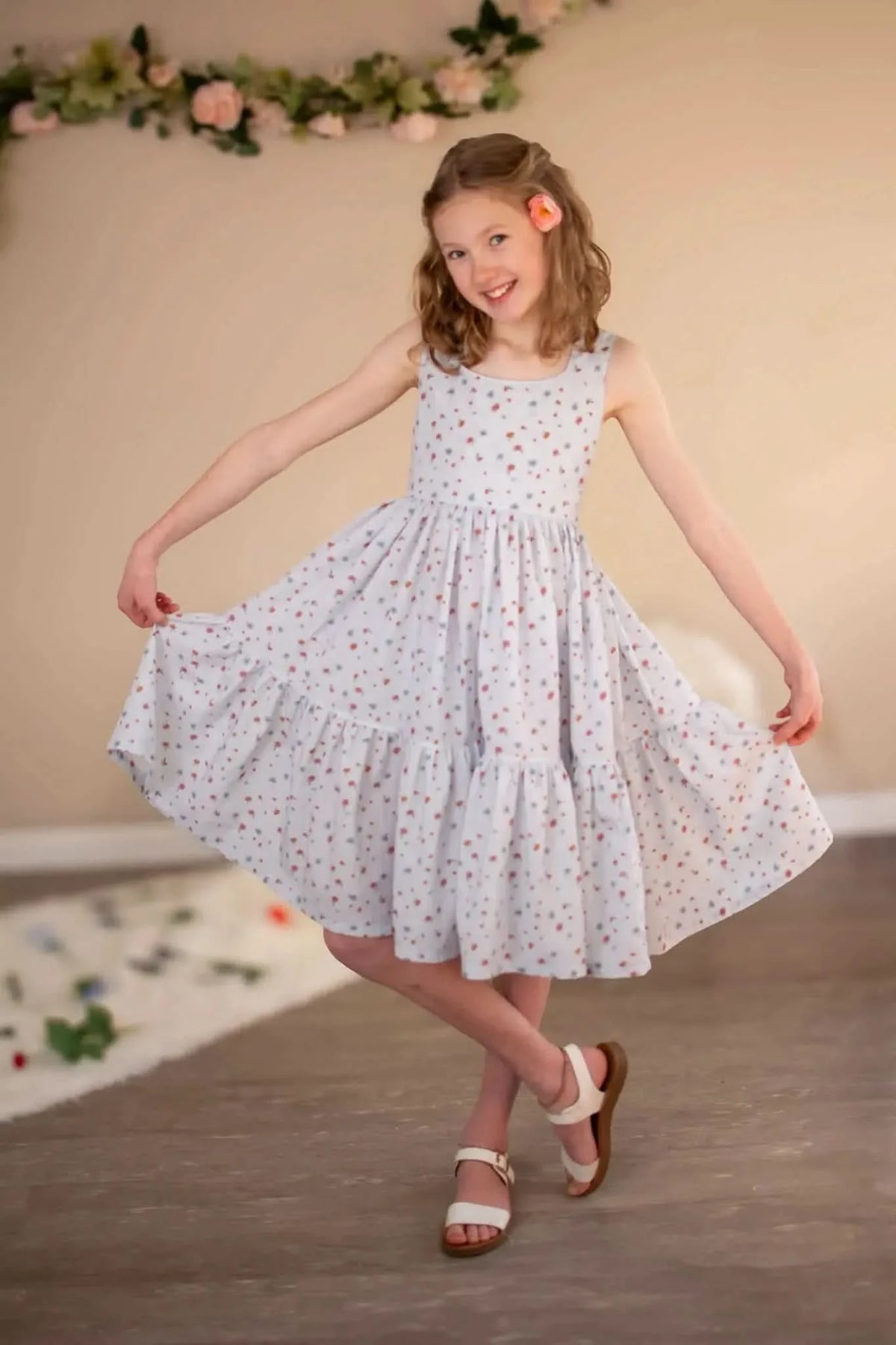 A young girl in a light blue floral dress with ruffles, holding out the skirt.