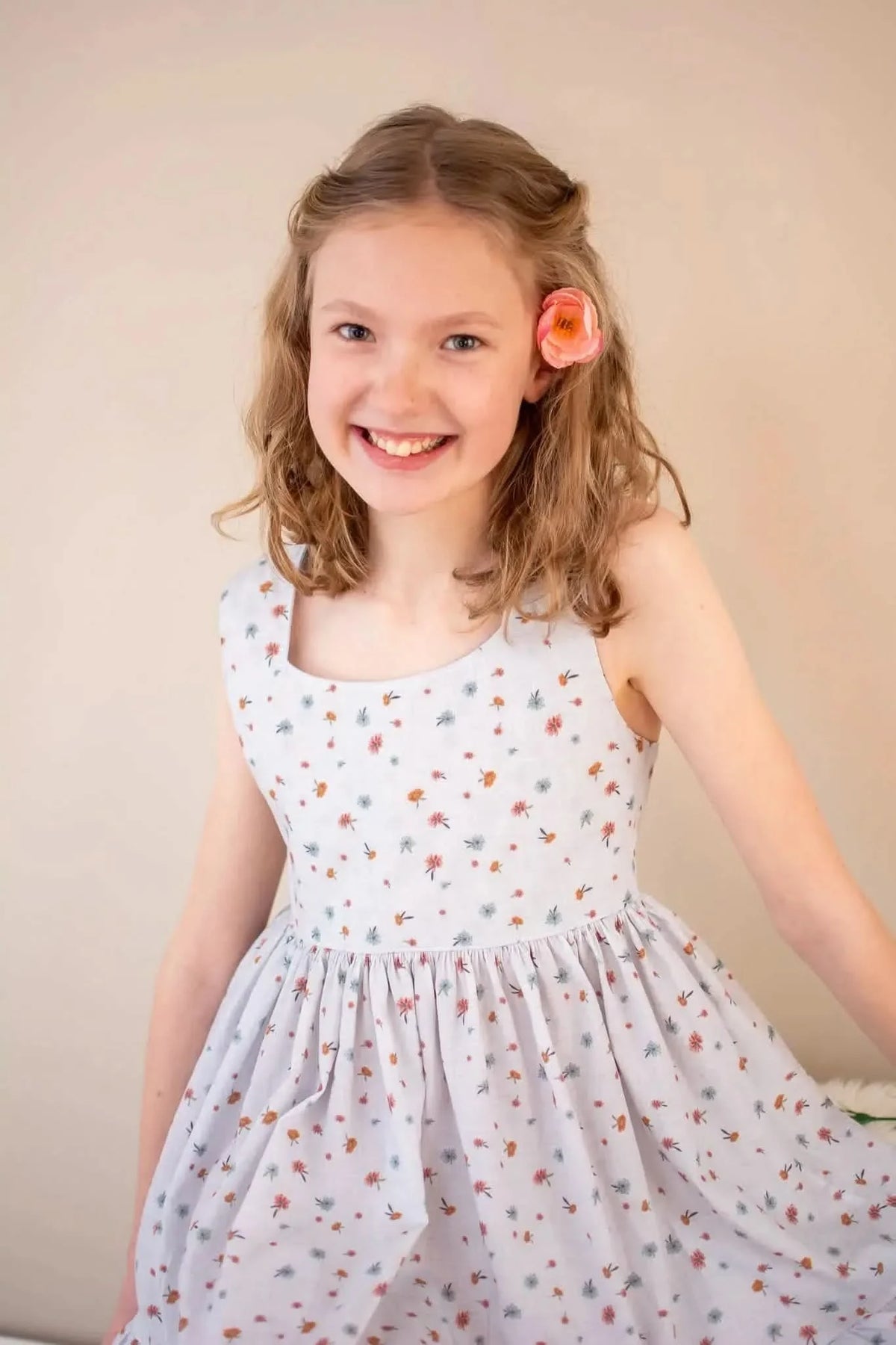 A young girl smiles, wearing a light blue dress with small floral patterns.