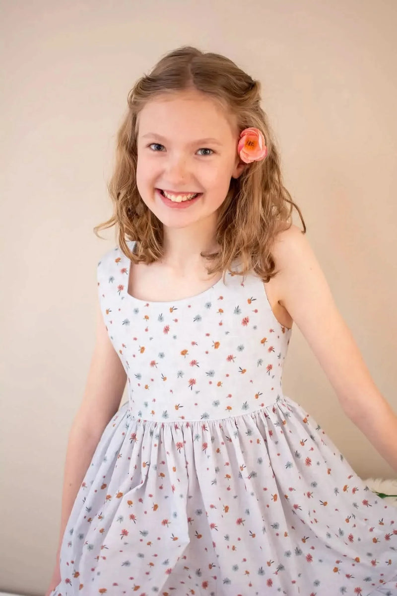 A young girl smiles, wearing a light blue dress with small floral patterns.