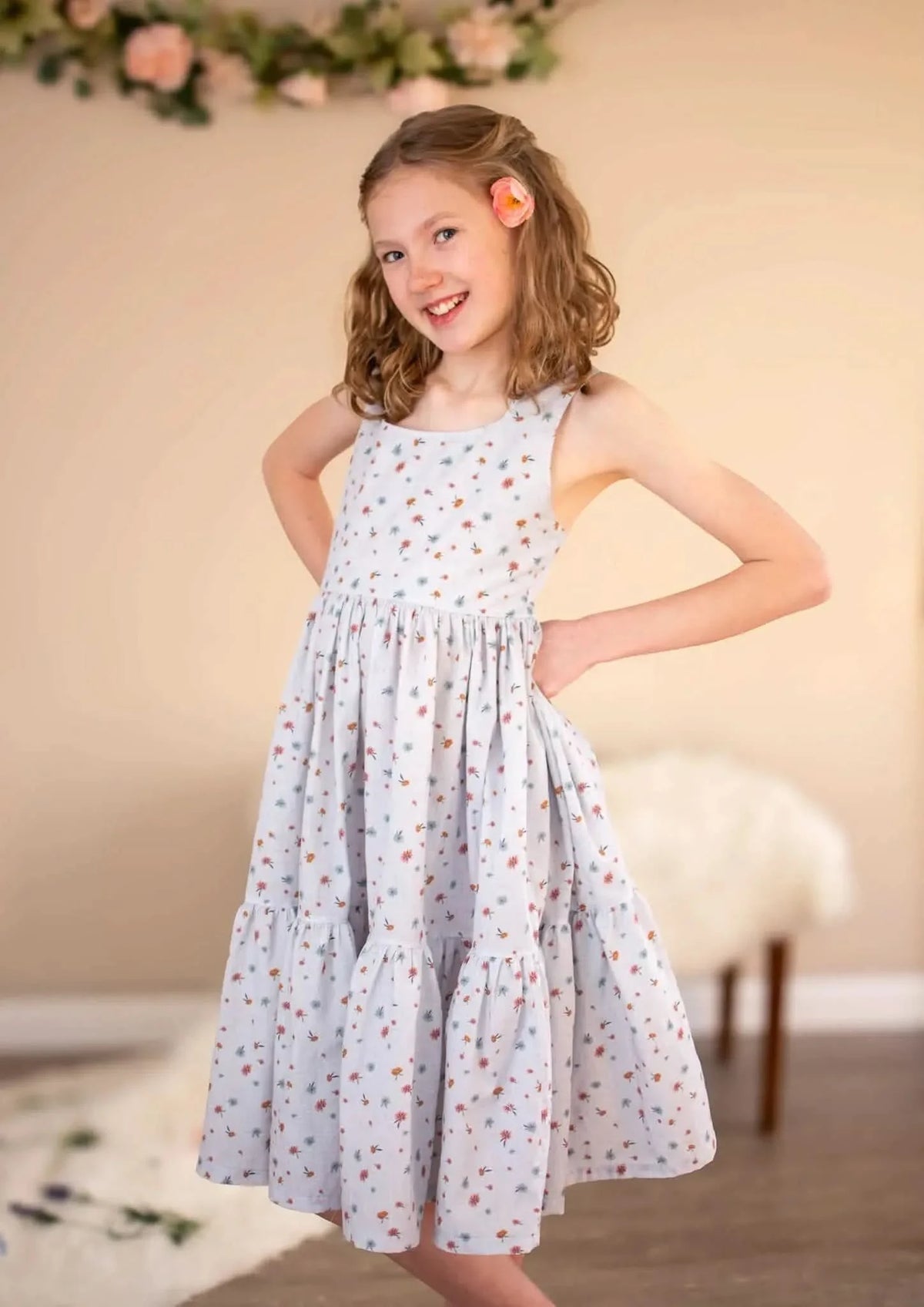 A young girl in a light blue floral dress with a tiered skirt and a pink flower in her hair.