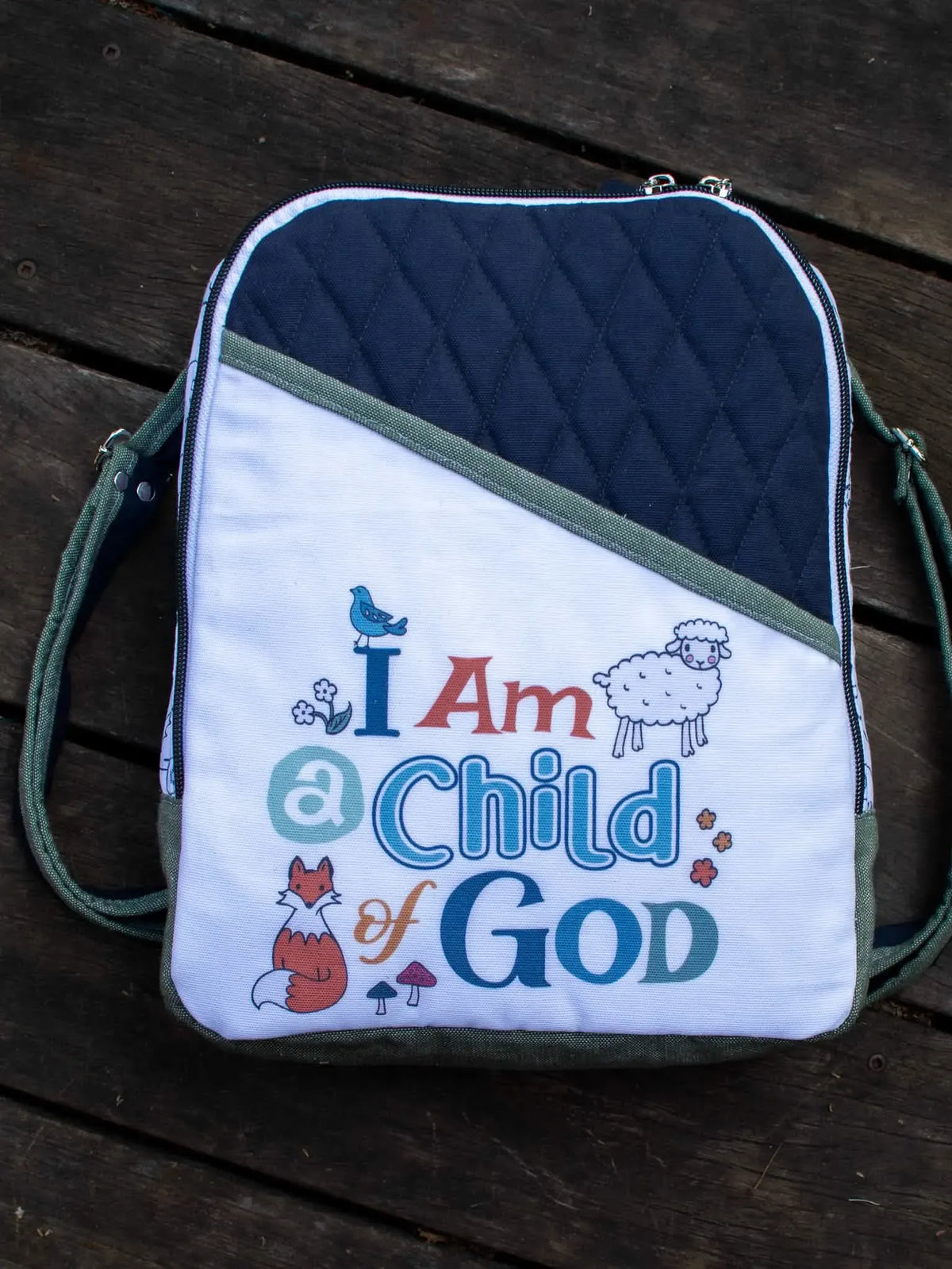 A white and navy quilted bag with "I Am a Child of God" and animal illustrations.