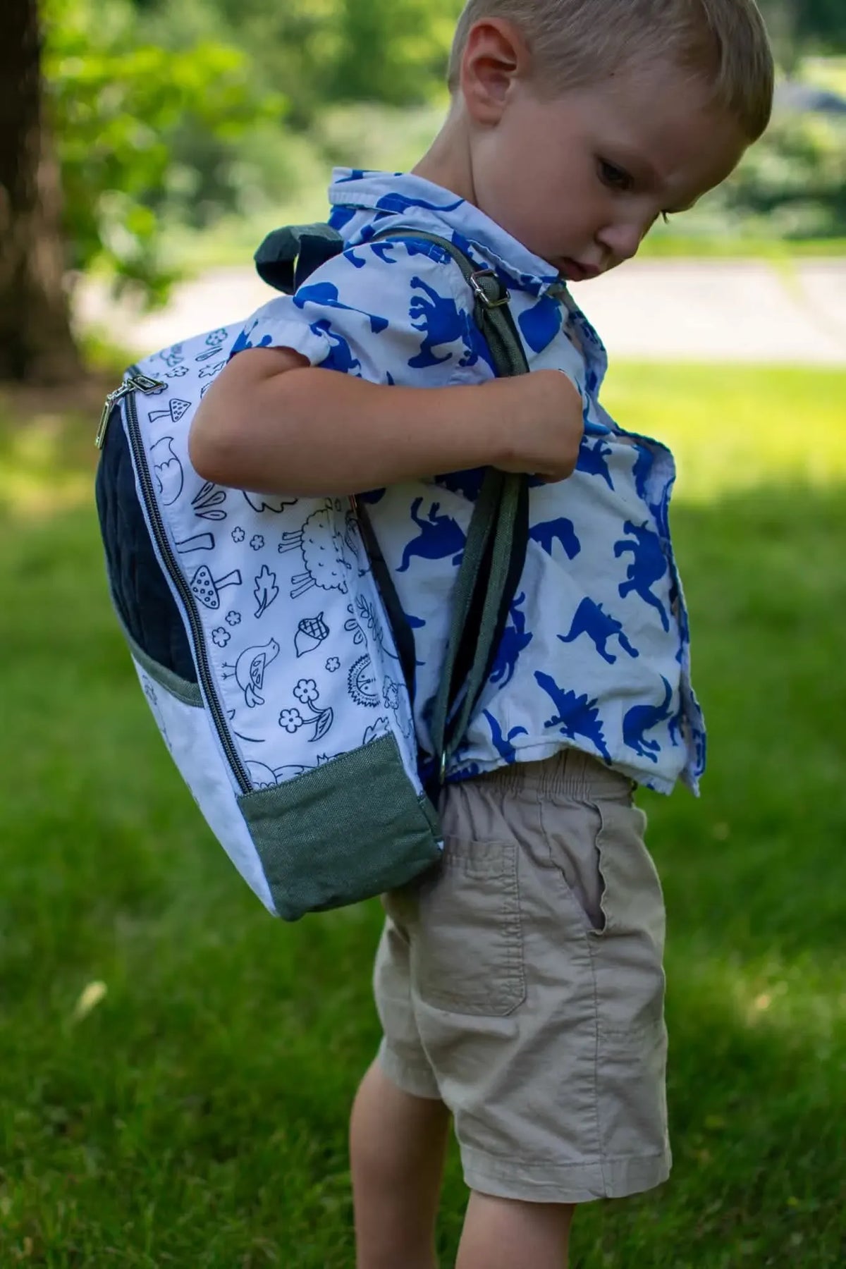 A young boy carries a backpack with a white panel featuring black woodland creature outlines.