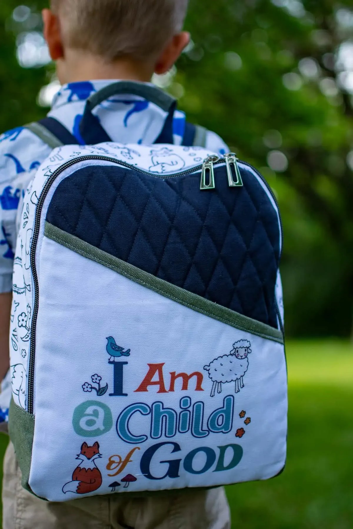 A child wears a backpack with "I Am a Child of God" and woodland creatures.