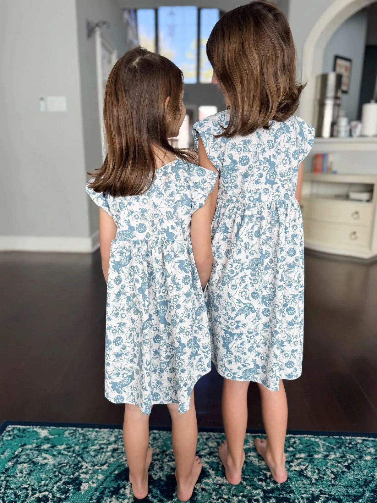 Two girls in matching blue and white floral dresses with bunny patterns.