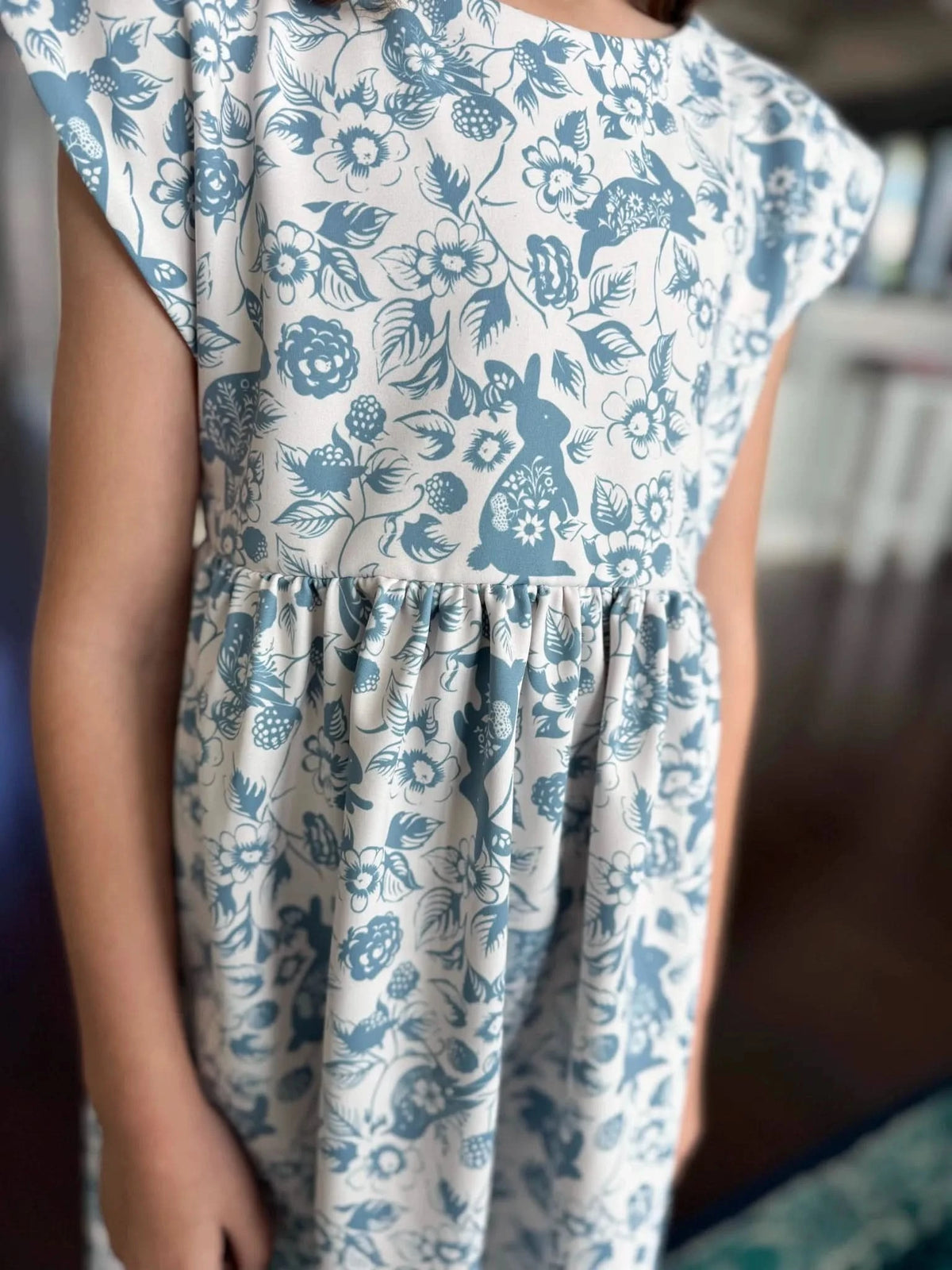 A child wears a dress with a blue and white bunny and floral pattern.