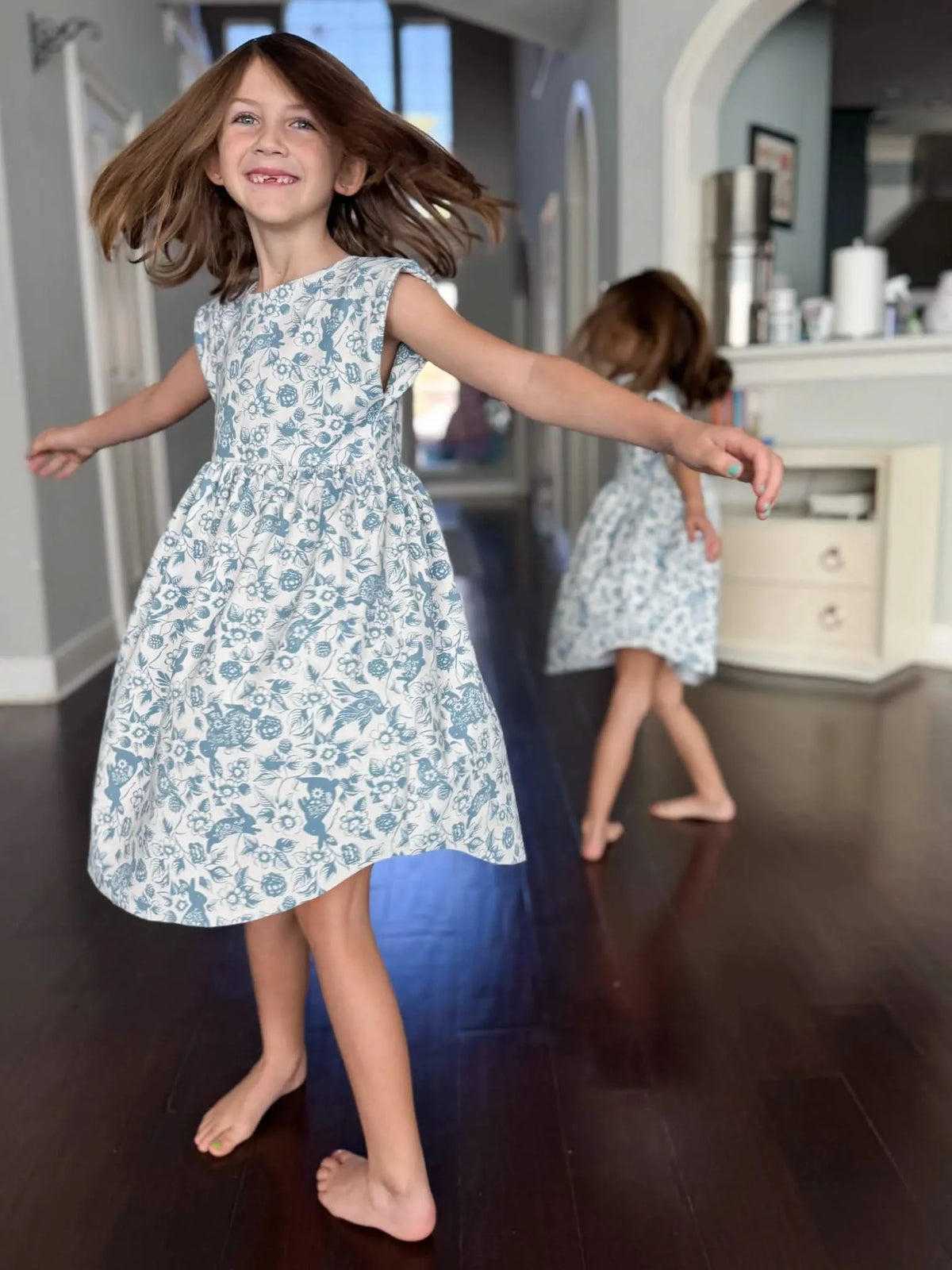 Two girls in blue and white bunny bramble dresses dance on a dark wood floor.