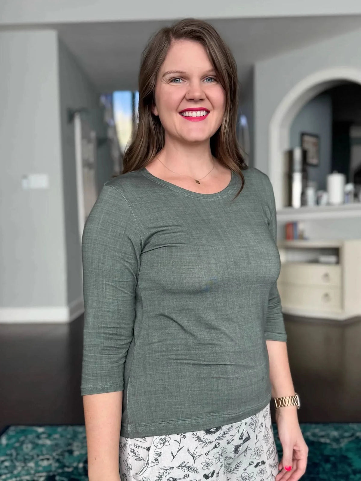 A woman wears an olive green long-sleeved shirt and patterned pants.