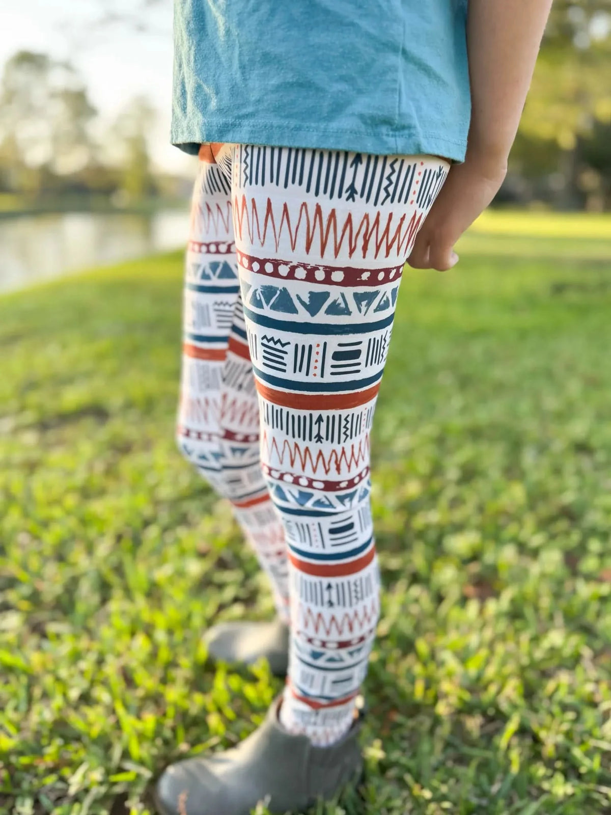 A person wears Desert Echoes patterned leggings and gray boots in a grassy field.