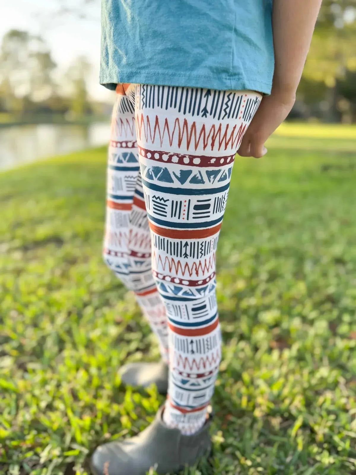 Close-up of legs wearing leggings with a geometric blue, white, and rust pattern on green grass.