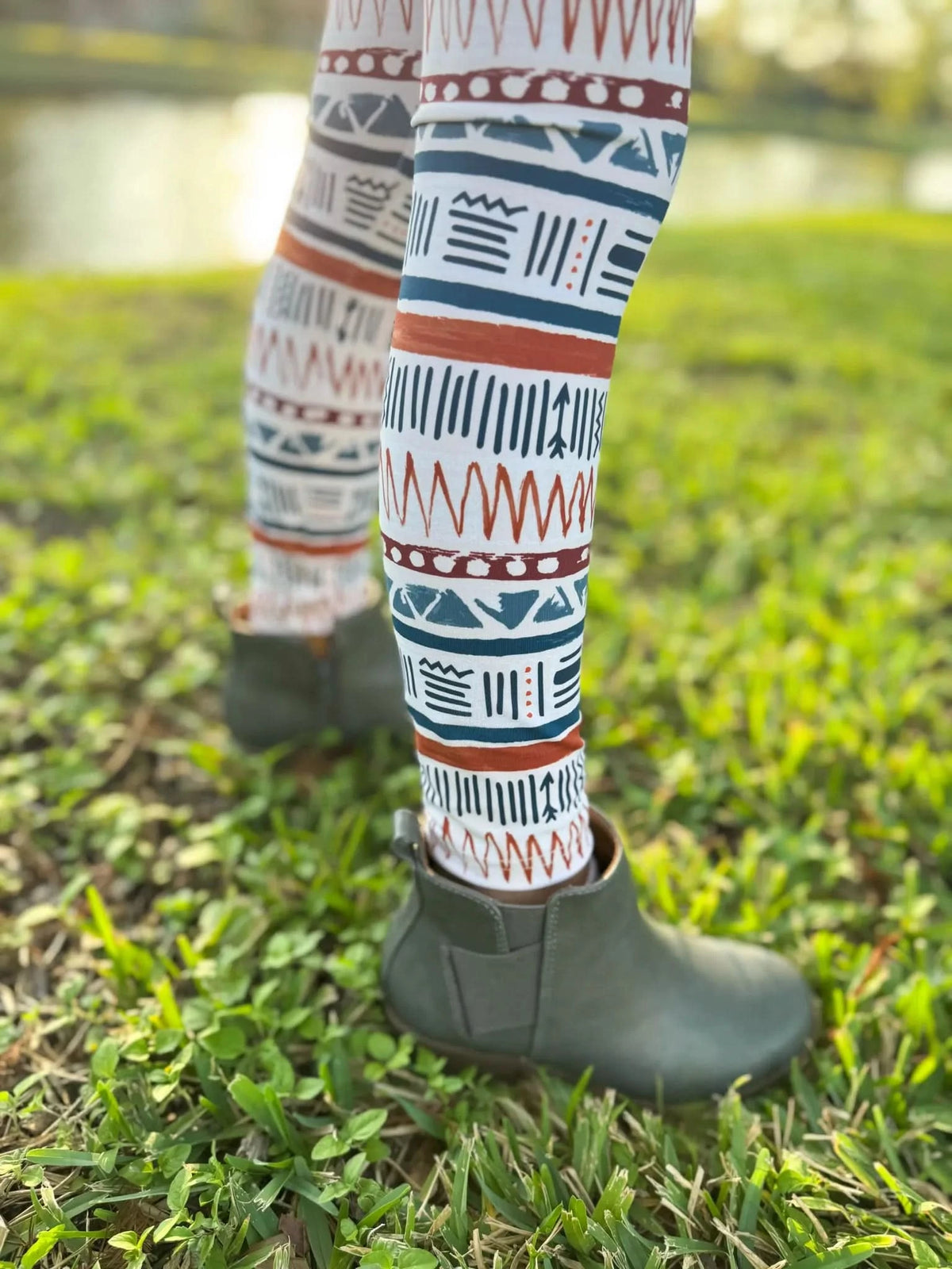 Legs wearing Desert Echoes patterned leggings and green boots stand on grass.