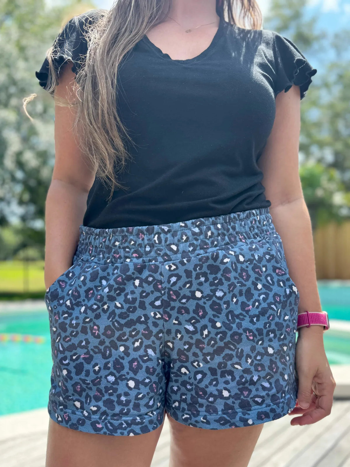 A person wears blue leopard print shorts and a black ruffled sleeve top.