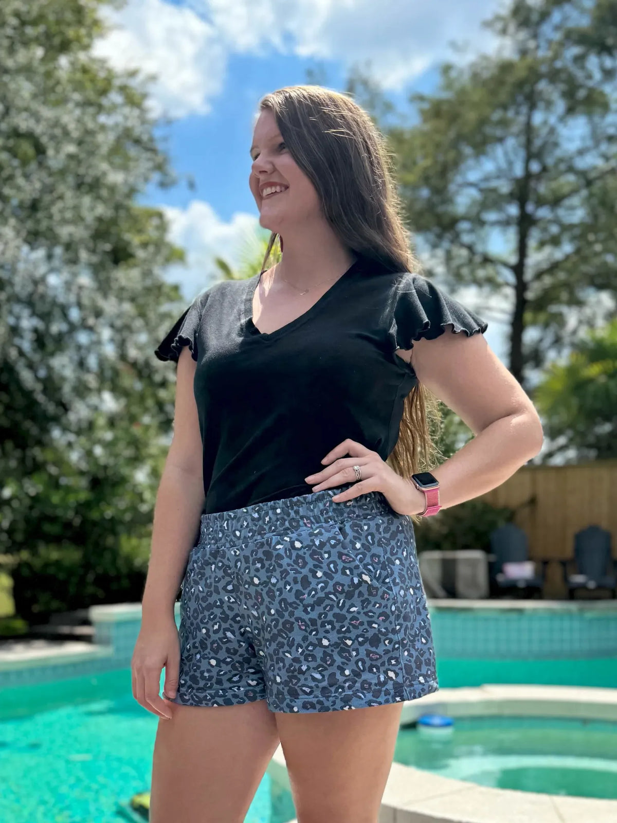 A woman wears blue leopard print shorts and a black v-neck shirt by a pool.