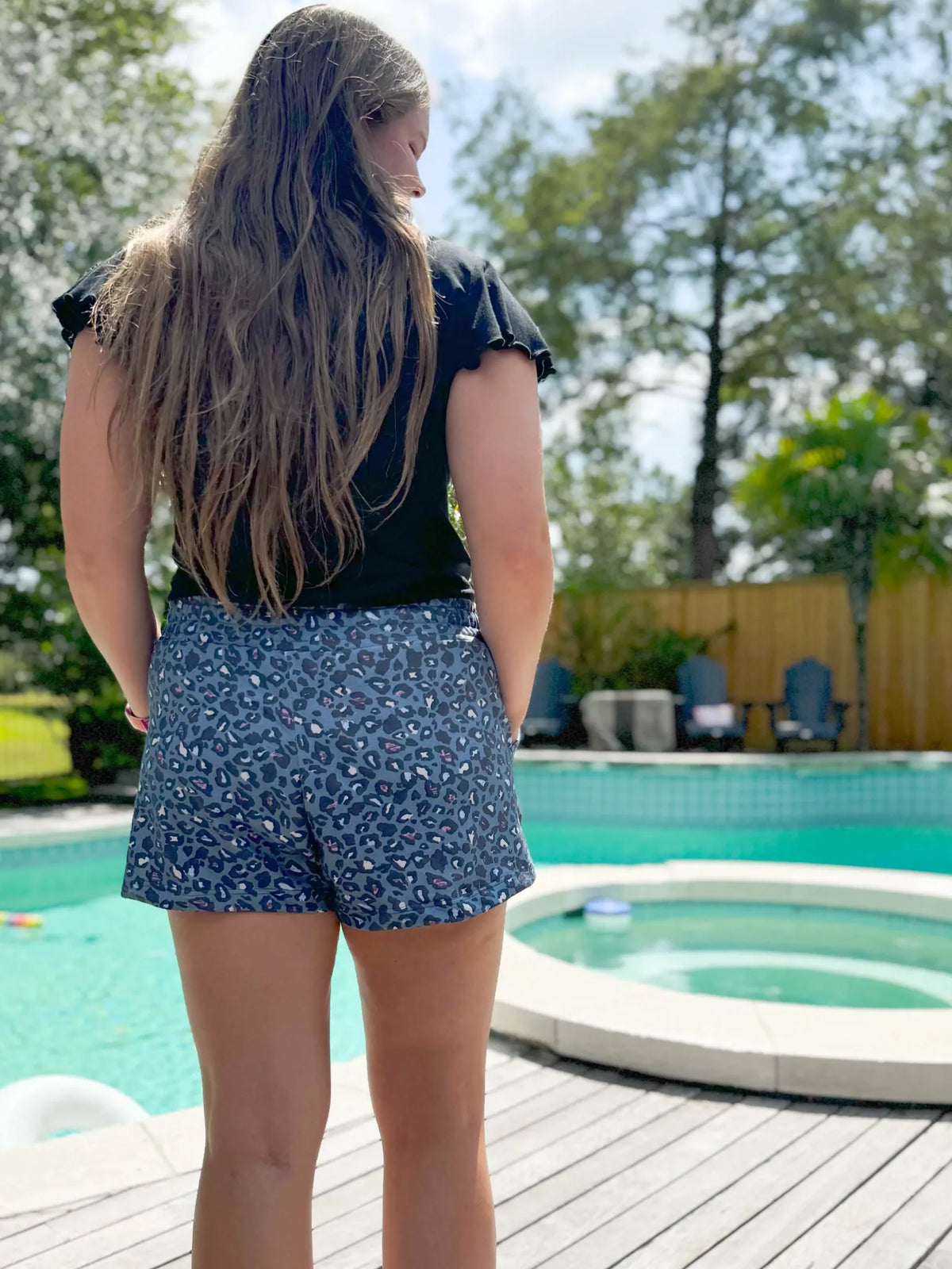 A person from behind wears blue leopard print shorts by a pool.