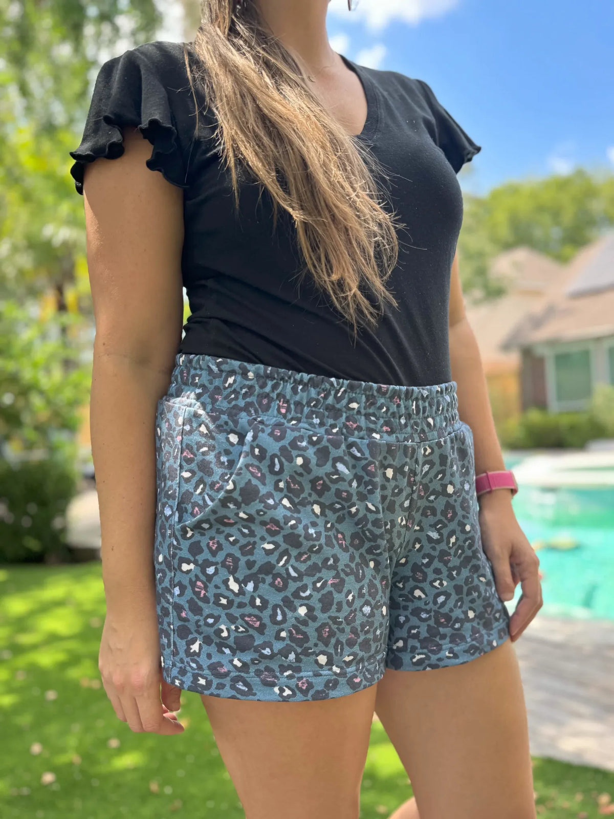 A person wears teal leopard print shorts and a black top outdoors.