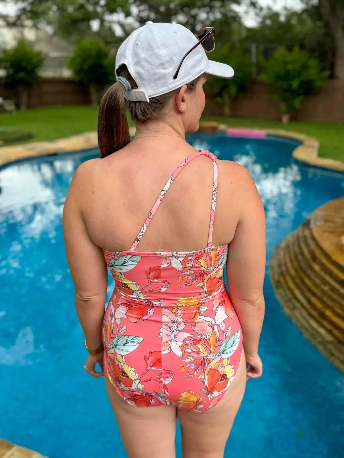 Rear view of a woman in a floral one-shoulder swimsuit made from Coral Memories fabric by a pool.