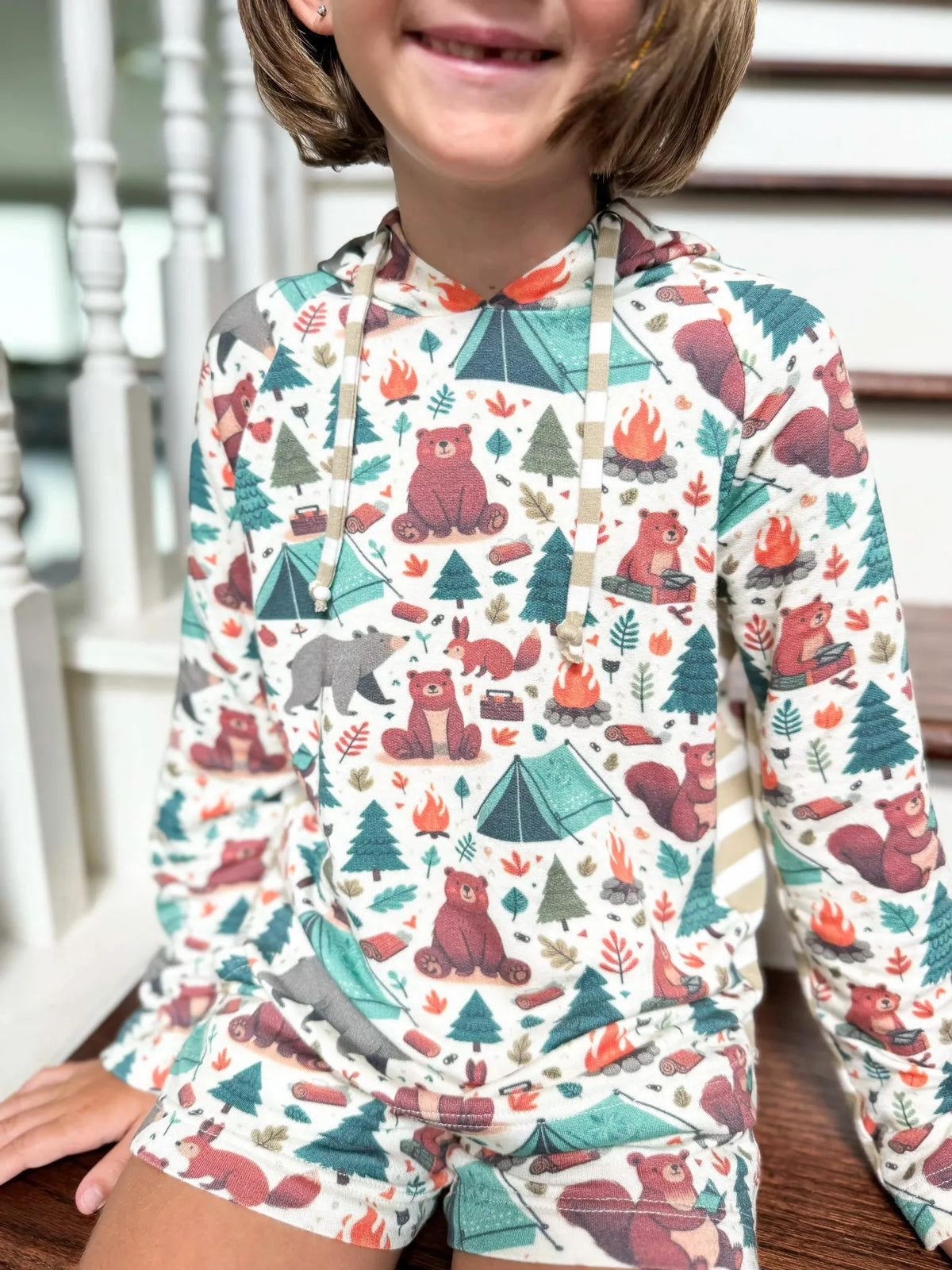Child wearing a hoodie and shorts with a camping bears print.