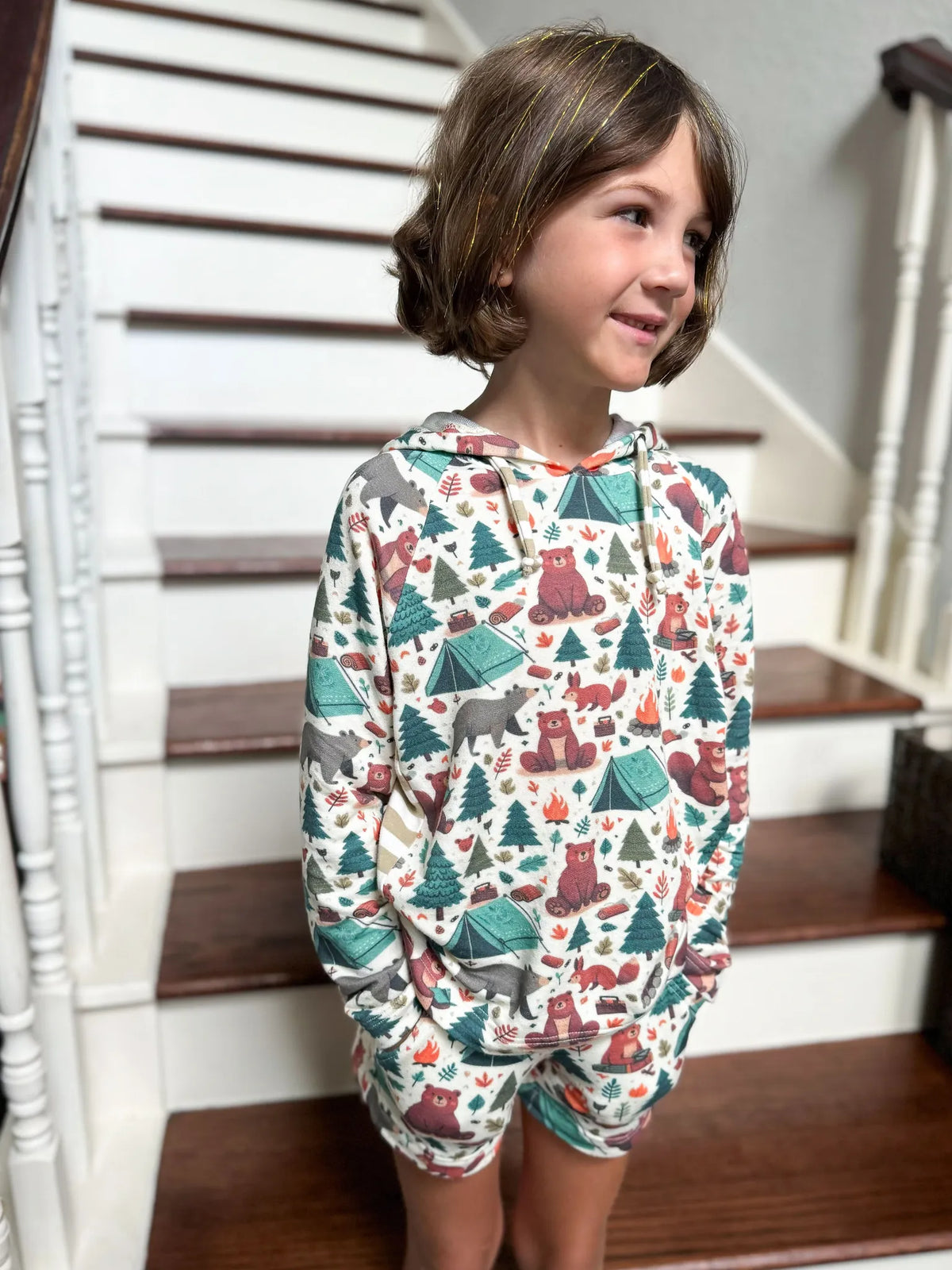 A child wears a hoodie and shorts with a camping bears pattern.
