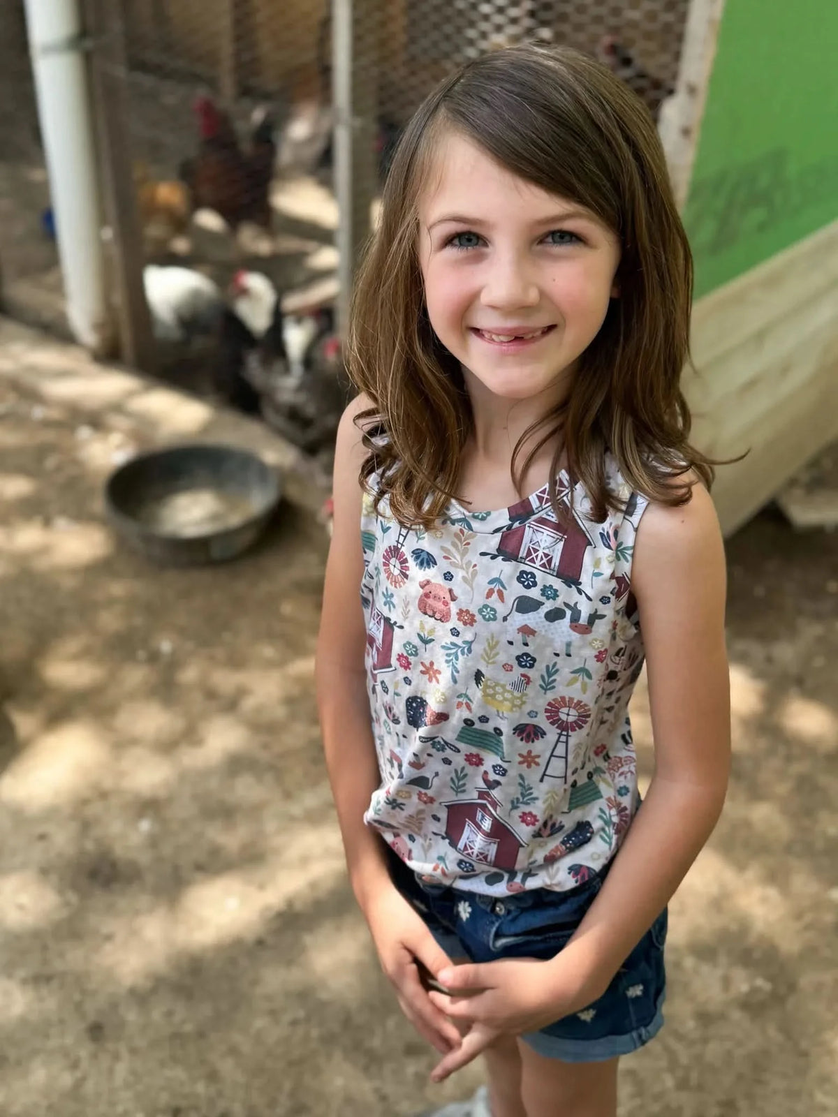 A young girl smiles, wearing a tank top with a colorful barnyard animal print.