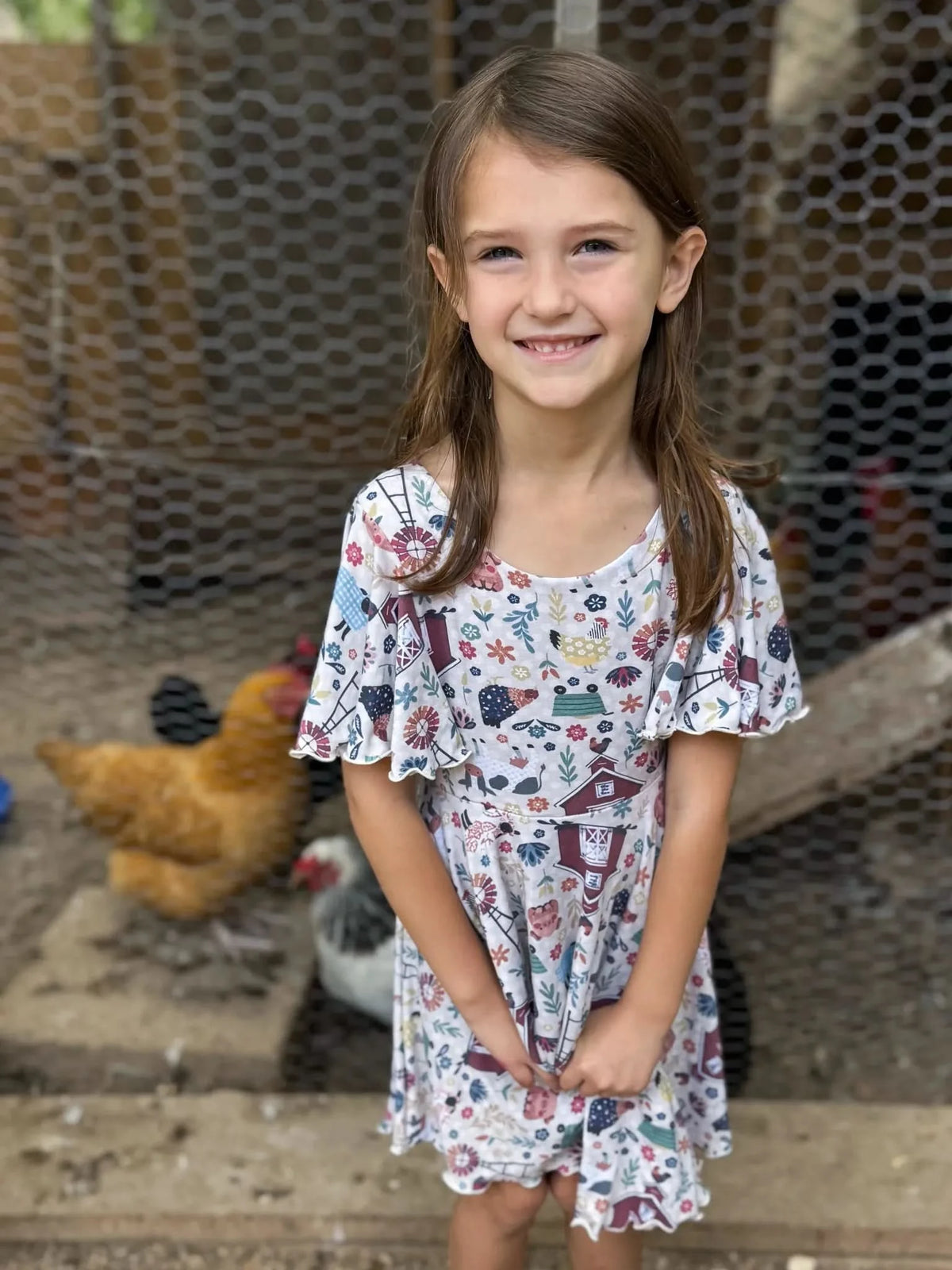 A young girl smiles, wearing a dress with a colorful barnyard print.