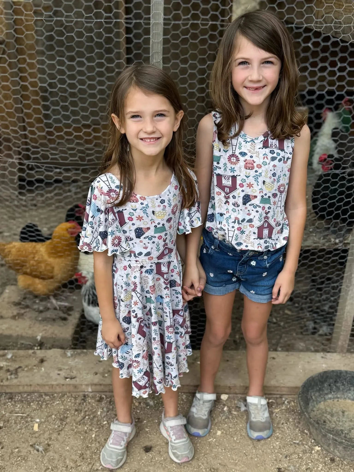 Two girls in matching farm-themed outfits stand in front of a chicken coop.